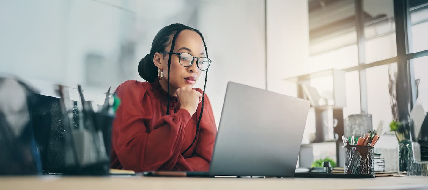 AI generated content image of a woman working on her laptop at her desk in an office with a window