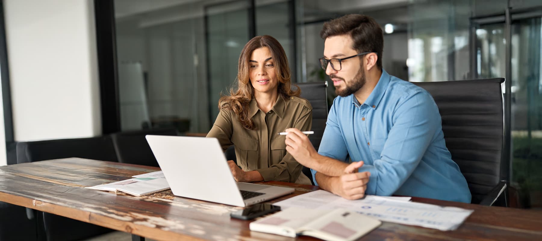 AI generated content image of a businessman and businesswoman reviewing documents and working on a laptop